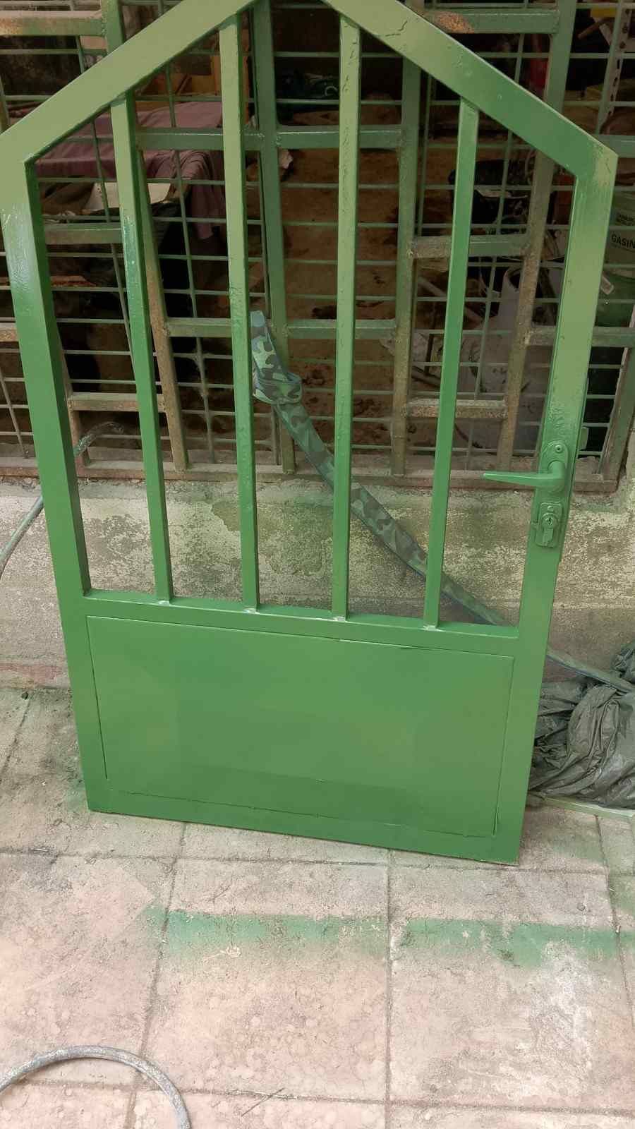 Una puerta metálica verde apoyada contra una valla en un sendero exterior embaldosado.