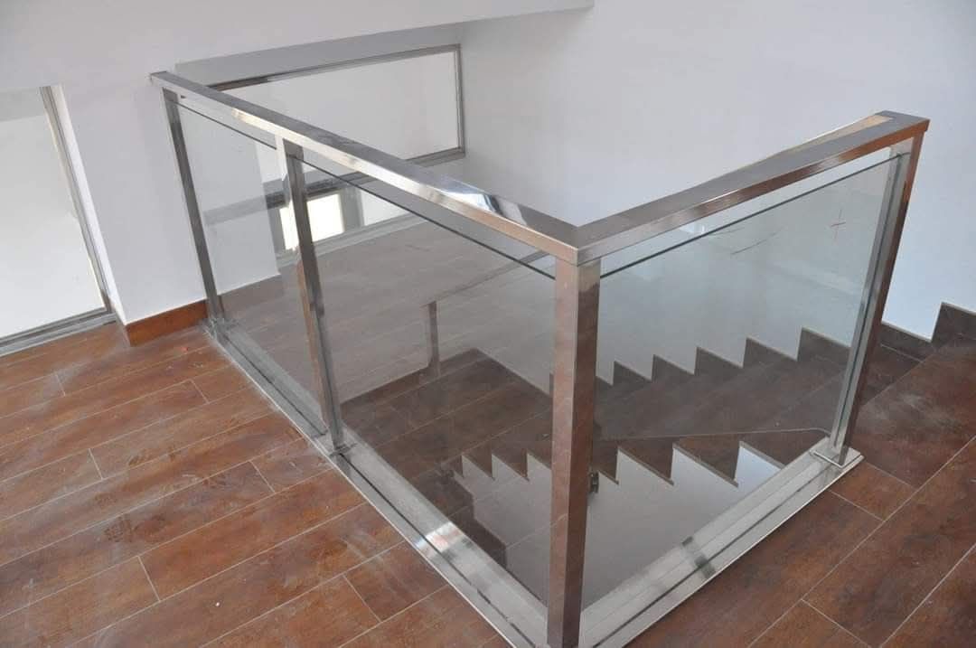 Escalera interior moderna con barandillas de vidrio y metal sobre un suelo de baldosas.