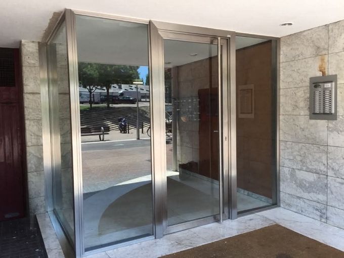 Entrada con puerta giratoria de cristal, paredes de mármol y acera reflejada en los paneles.