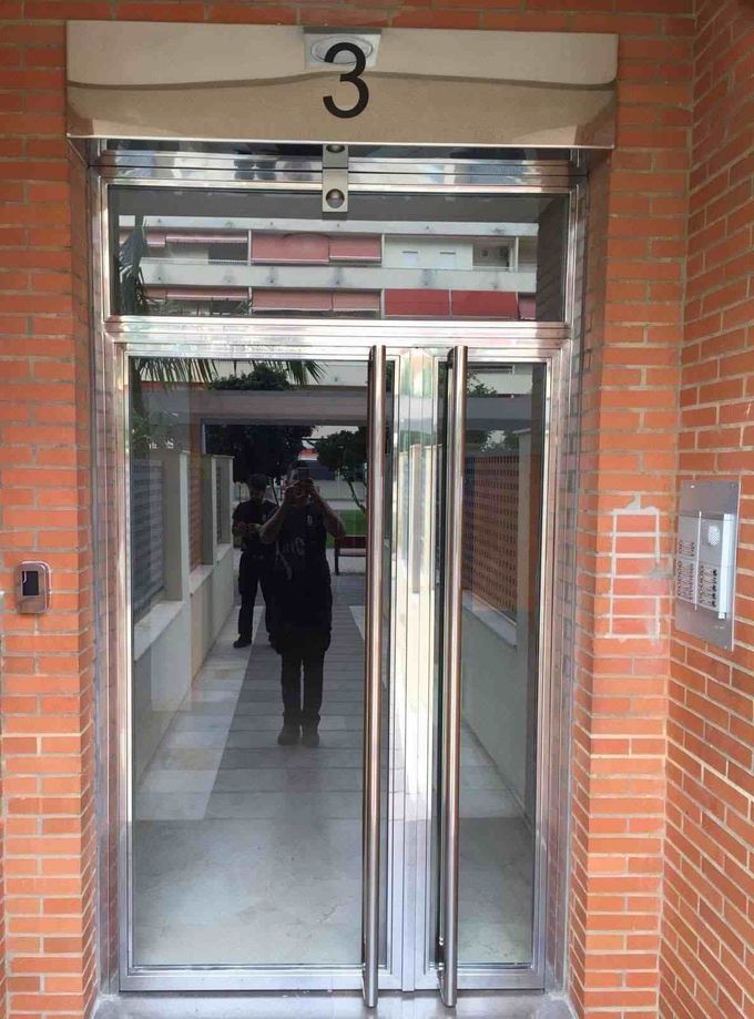 Entrada de ascensor de cristal con el número “3” en un edificio de ladrillo, con una persona reflejada en el interior.
