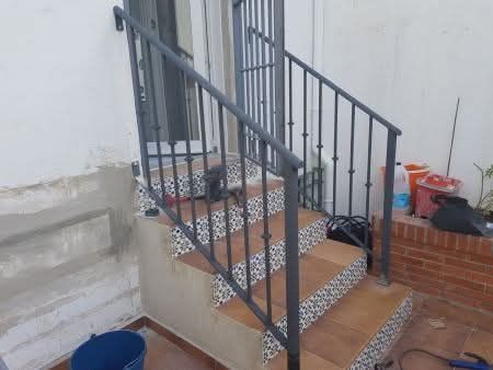 Escaleras exteriores de hormigón con barandillas metálicas y escalones de baldosas estampadas junto a una pared blanca.