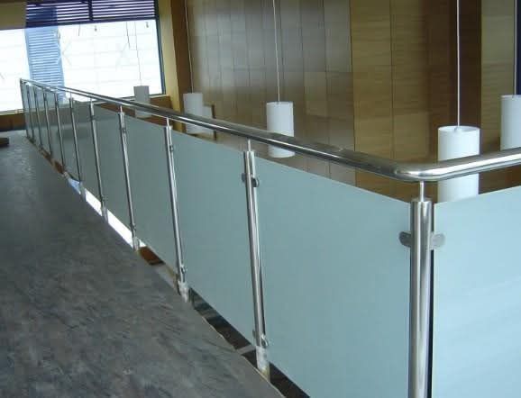 Pasillo interior con barandilla de vidrio esmerilado y pasamanos de metal junto a una pared alicatada.