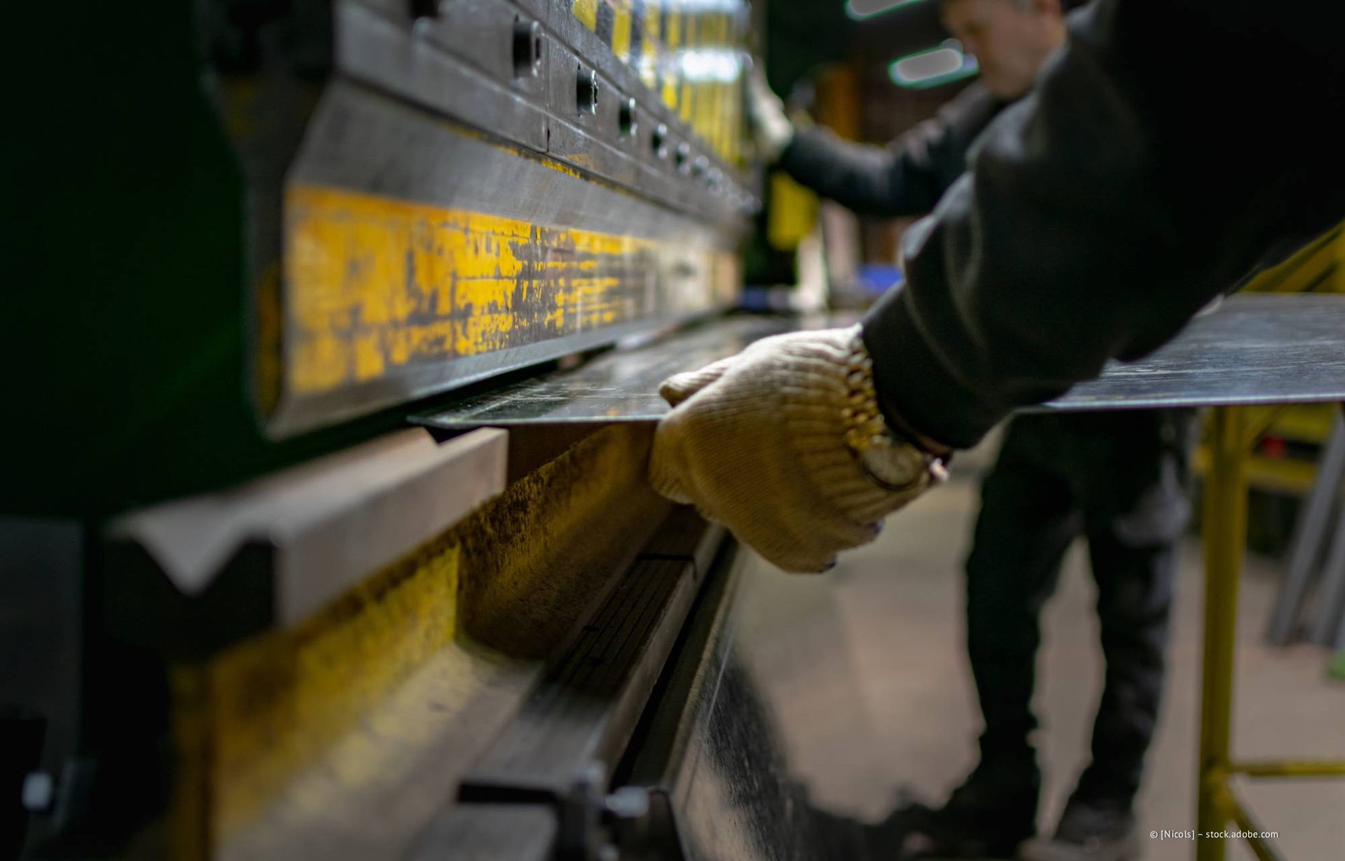 Ein Arbeiter mit Schutzhandschuhen biegt ein Metallblech mit einer großen Industriemaschine.