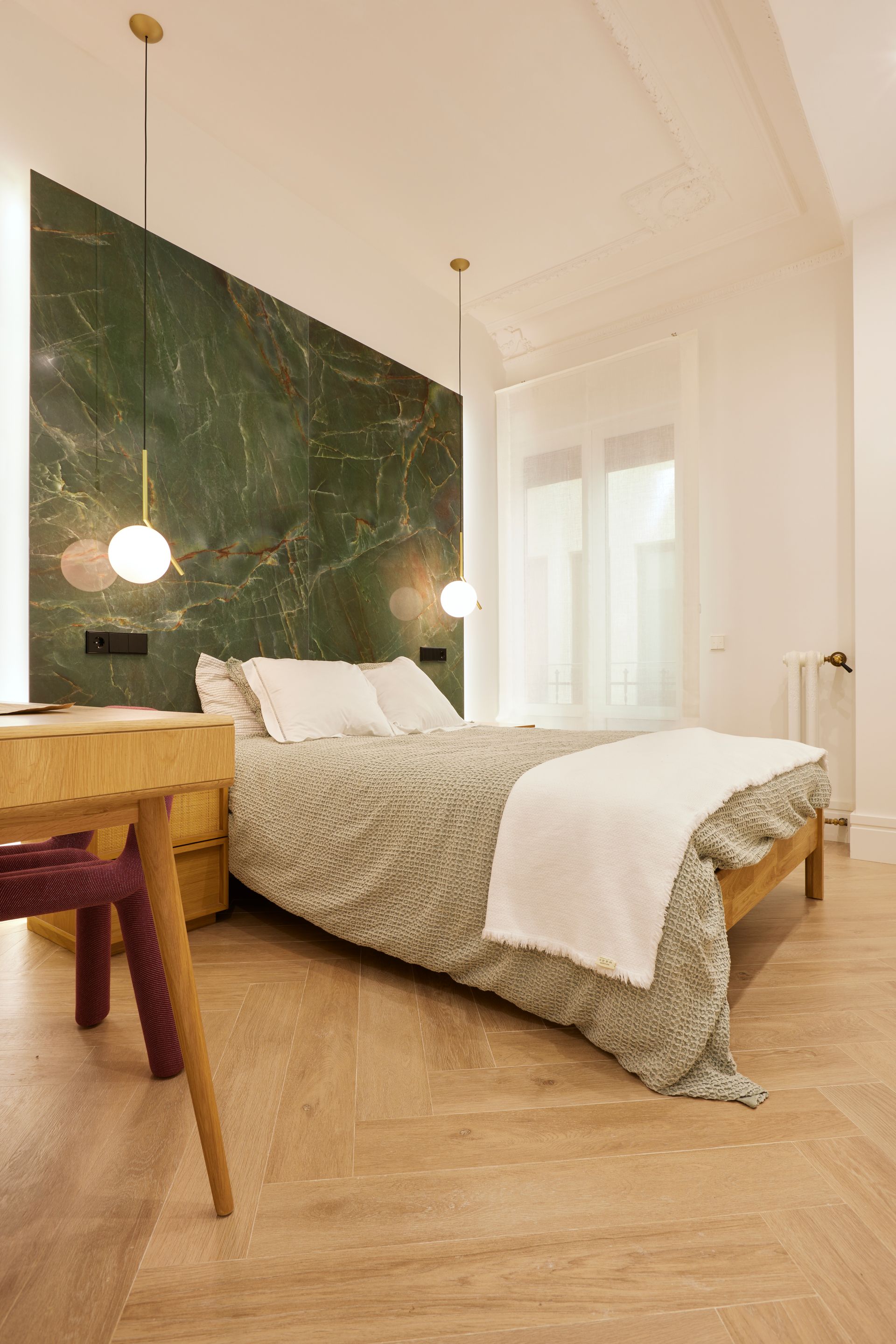 Un dormitorio con cama, escritorio, silla y pared de mármol verde.