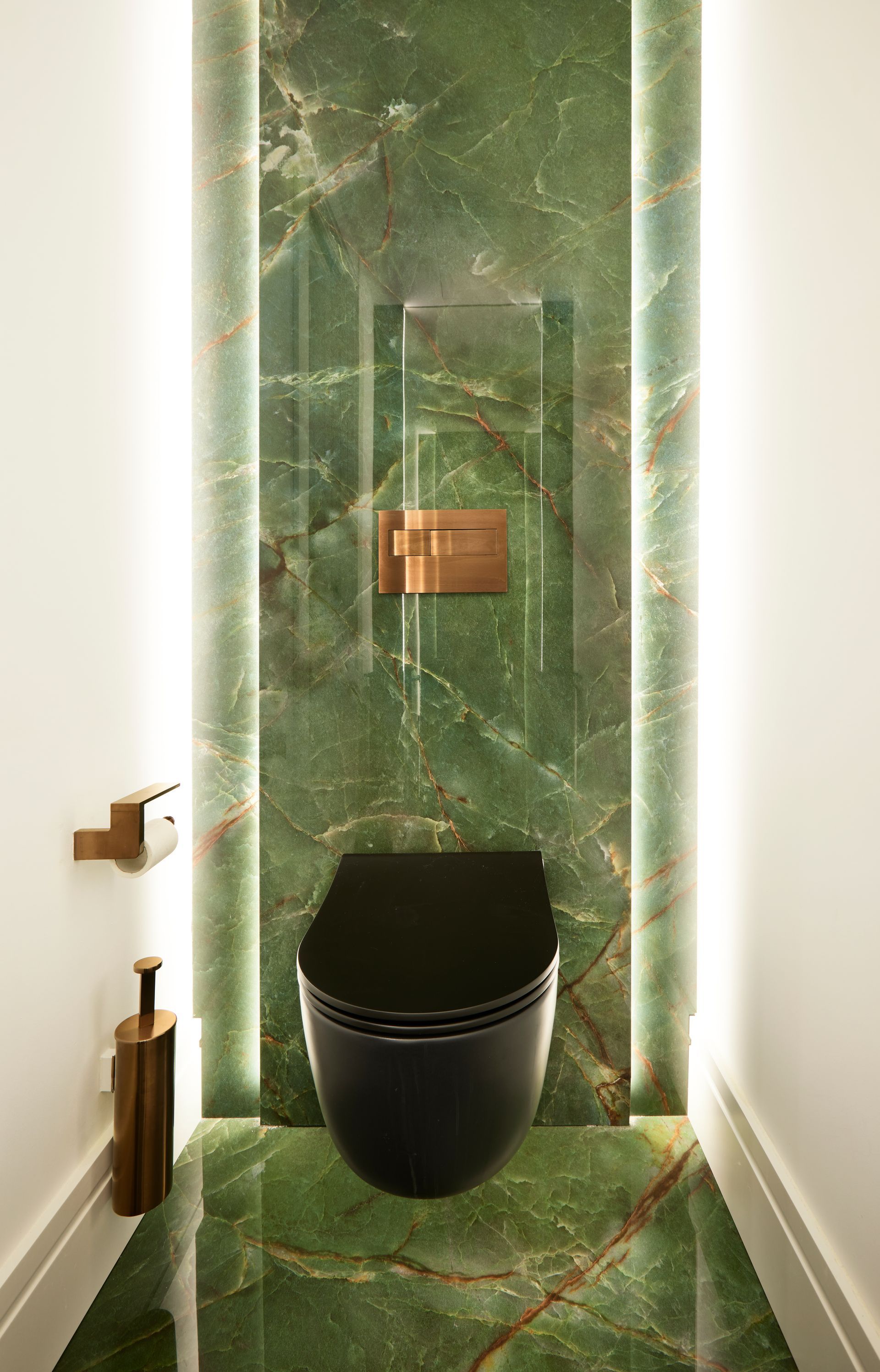 Un baño con inodoro negro y una pared de mármol verde.