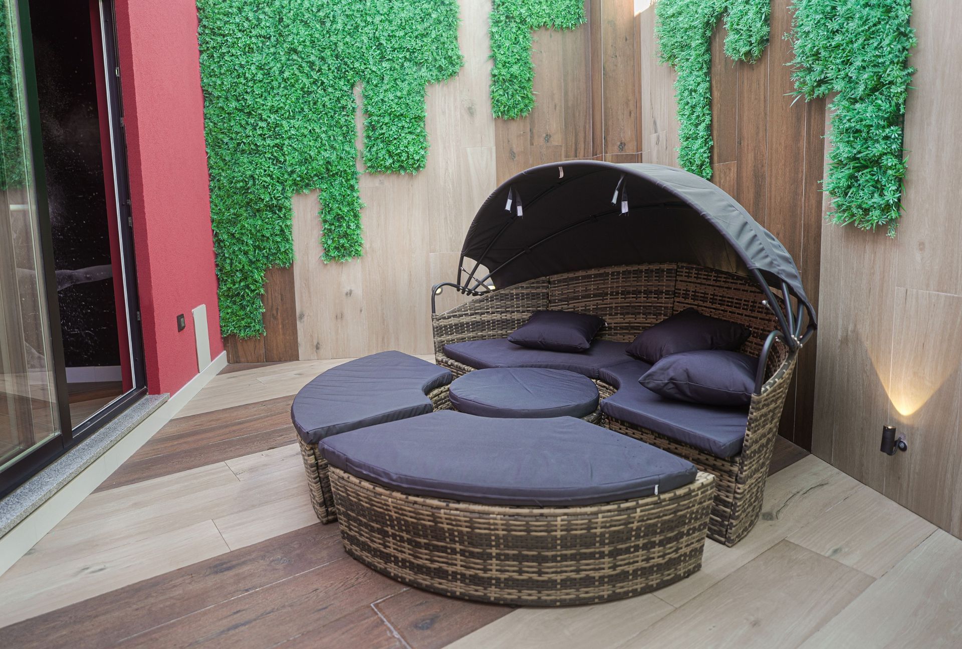 Un diván de mimbre con dosel se encuentra sobre un piso de madera en un patio.