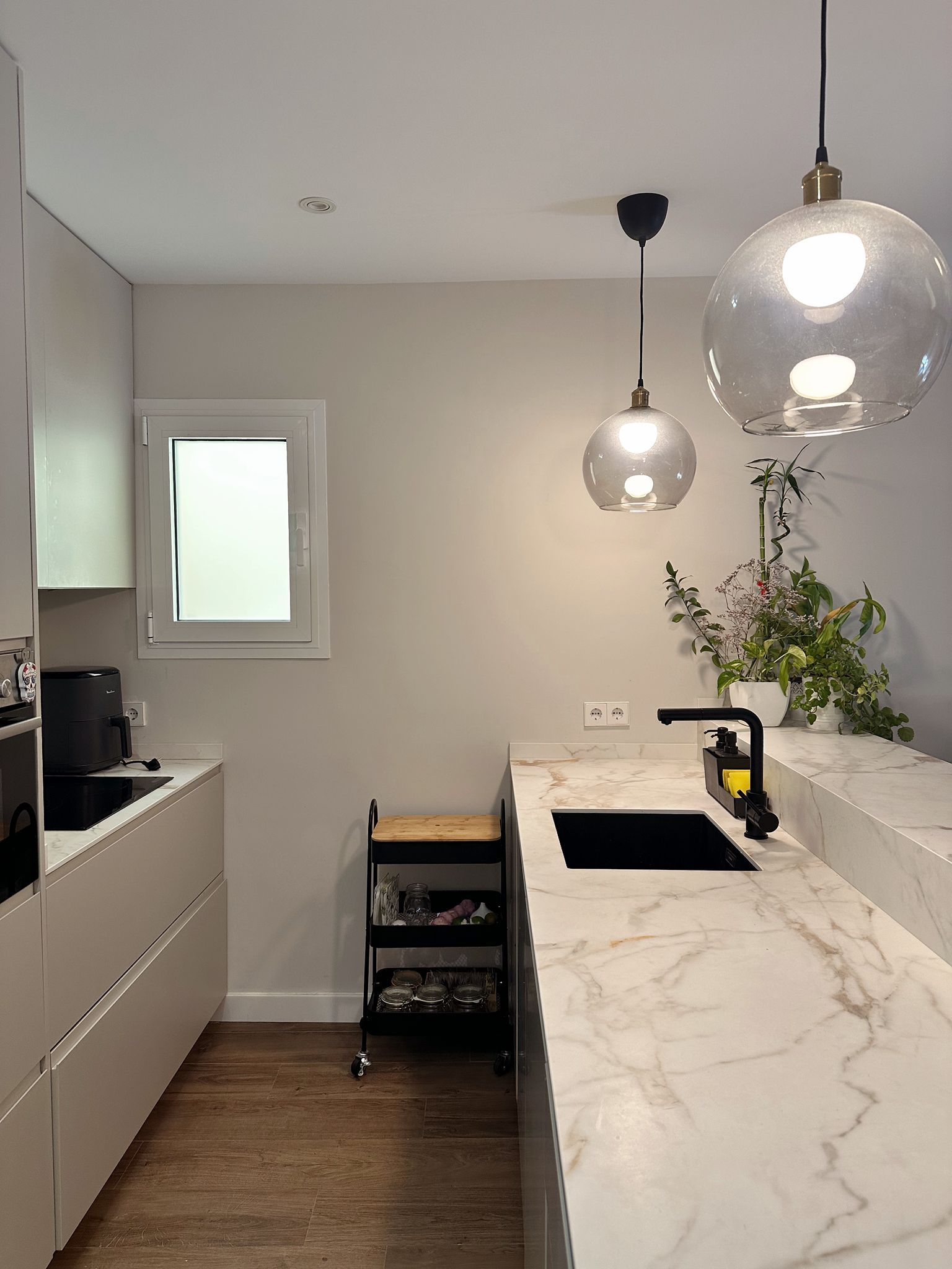 Una cocina con gabinetes blancos, encimeras de mármol, un fregadero y una ventana.