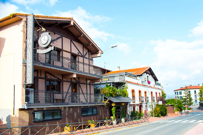 Edificio de varias plantas con fachada de madera y piedra, situado en una calle. Cielo azul de fondo.