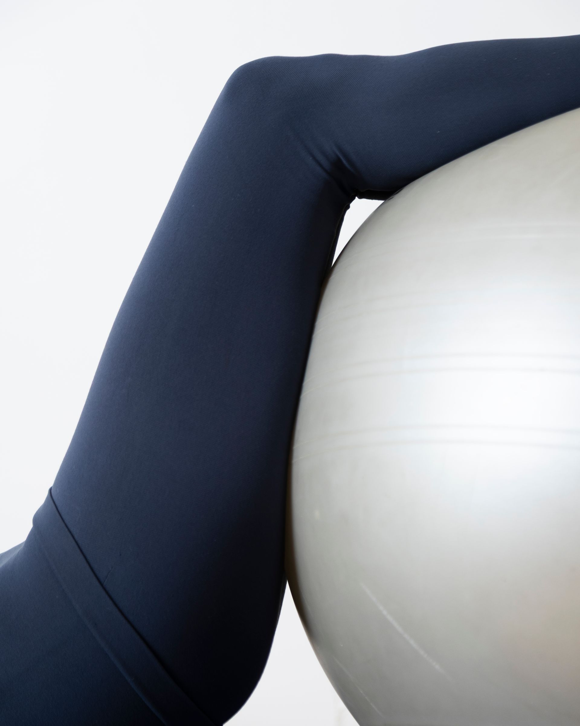La gamba dei leggings blu navy poggia su una palla da ginnastica argentata.