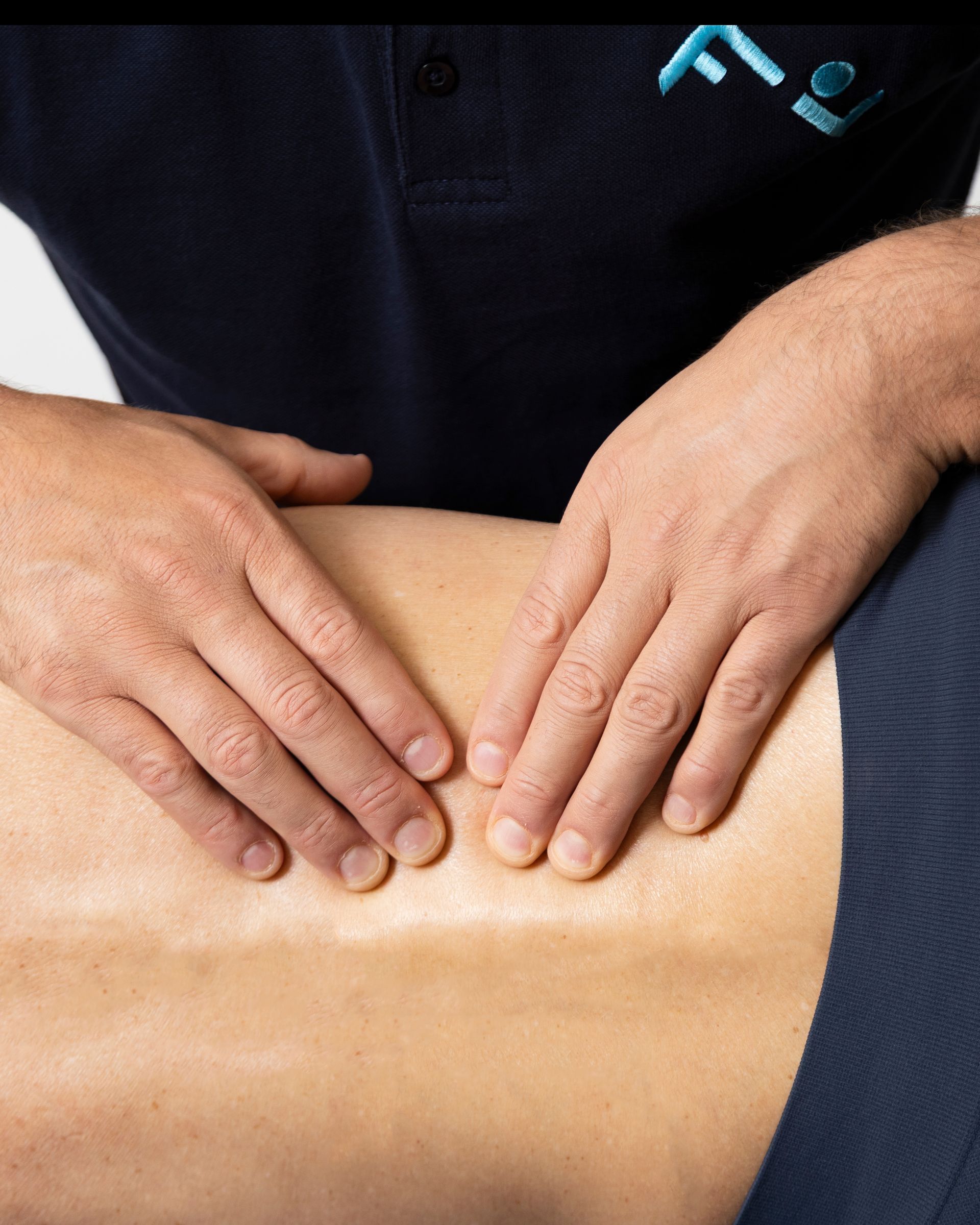 Mani che massaggiano la parte bassa della schiena di una persona. Pelle chiara, camicia blu scuro, sfondo neutro.