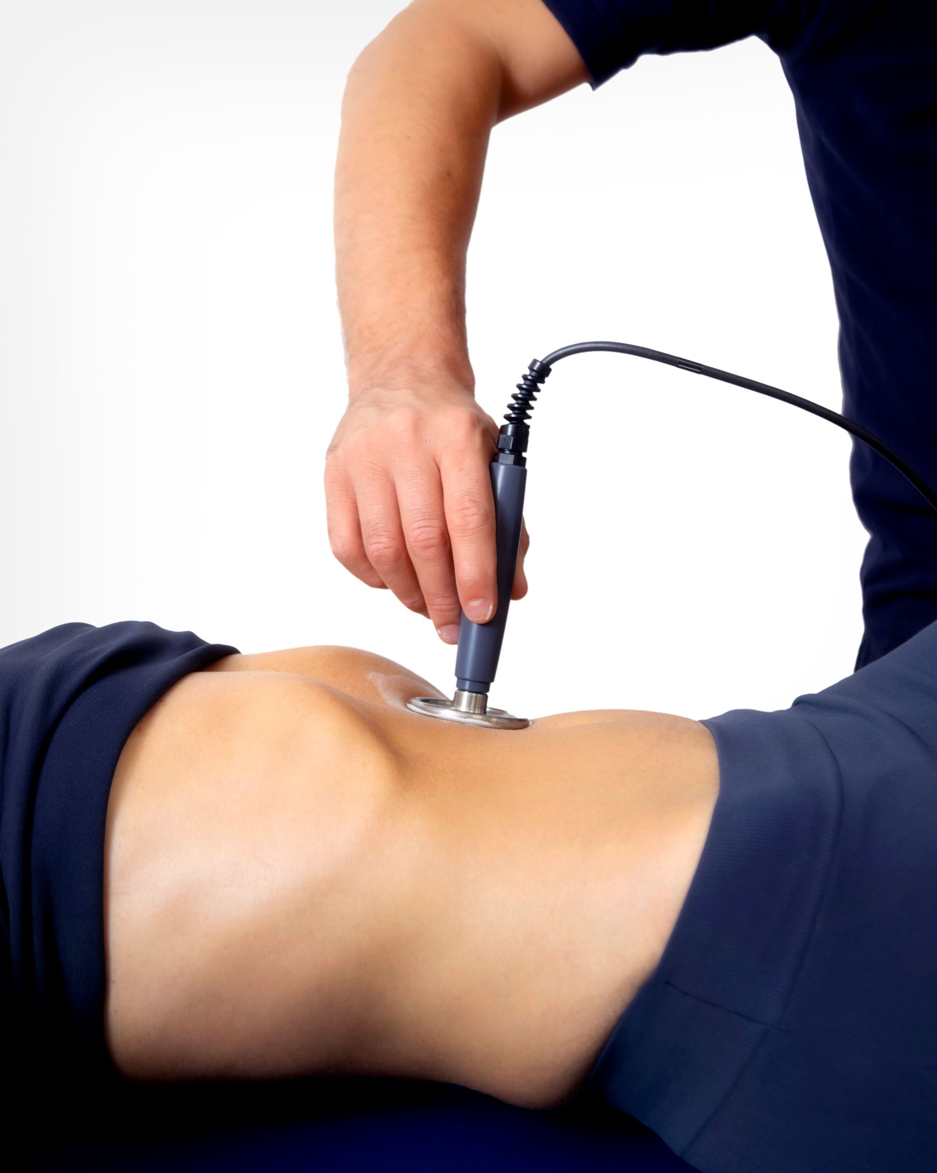 Terapista che utilizza un dispositivo medico sulla parte bassa della schiena di un paziente. Indumenti blu, sfondo bianco.