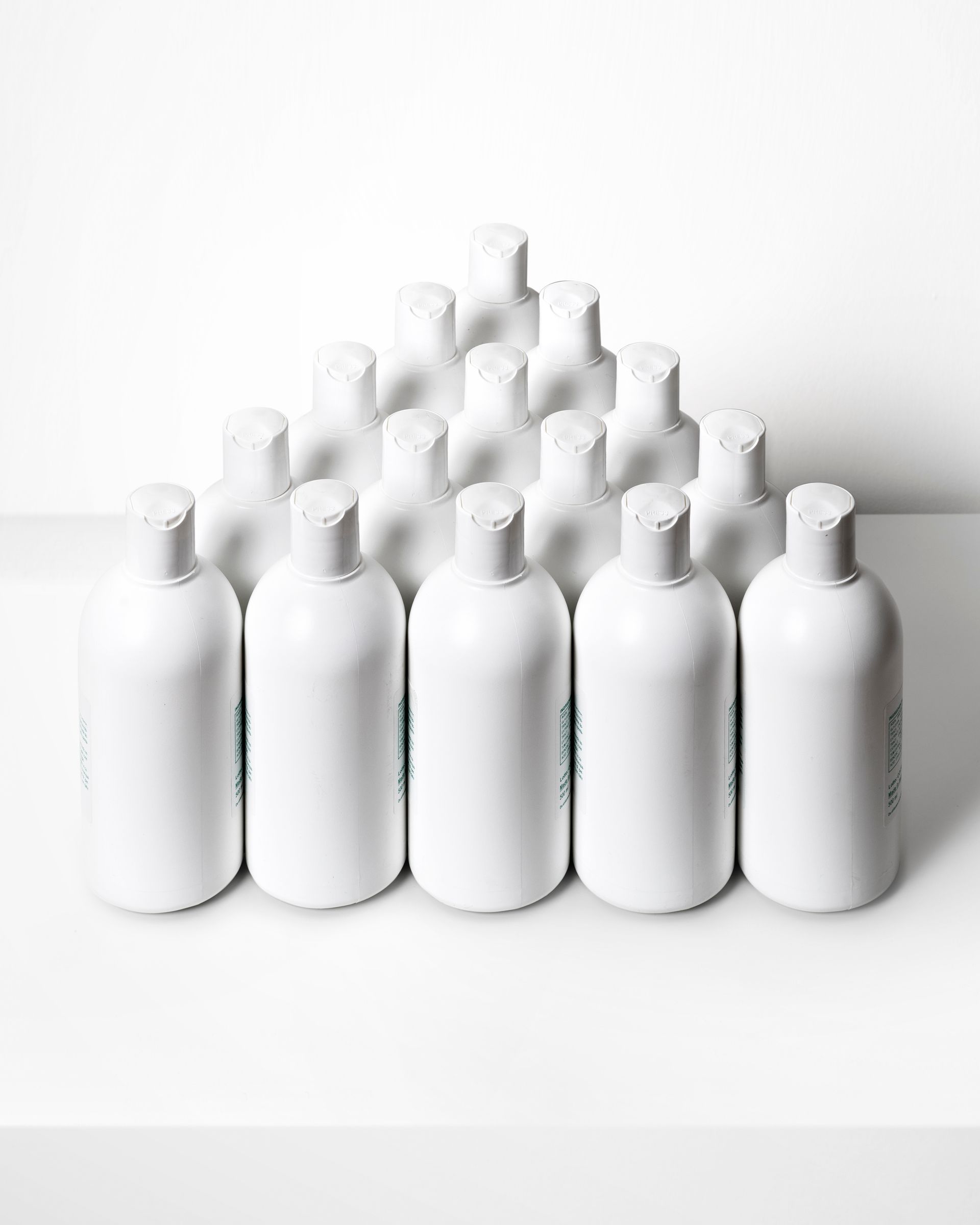 Bottiglie bianche disposte a forma di piramide su una superficie bianca.