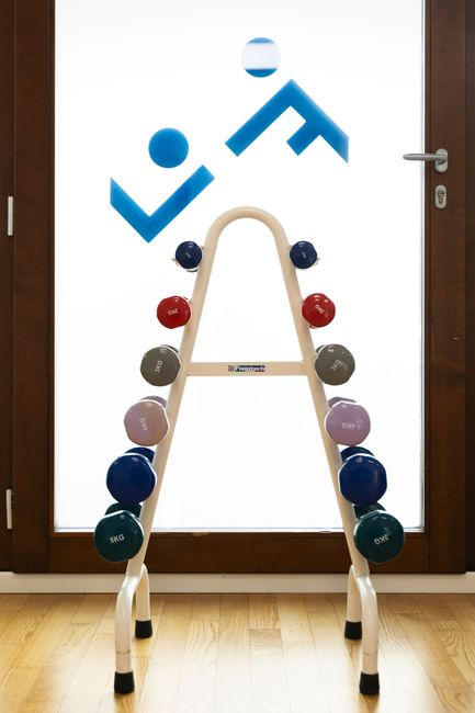 Un uomo con una polo nera è appoggiato a una panchina all'aperto. Sullo sfondo, un muro rosso.