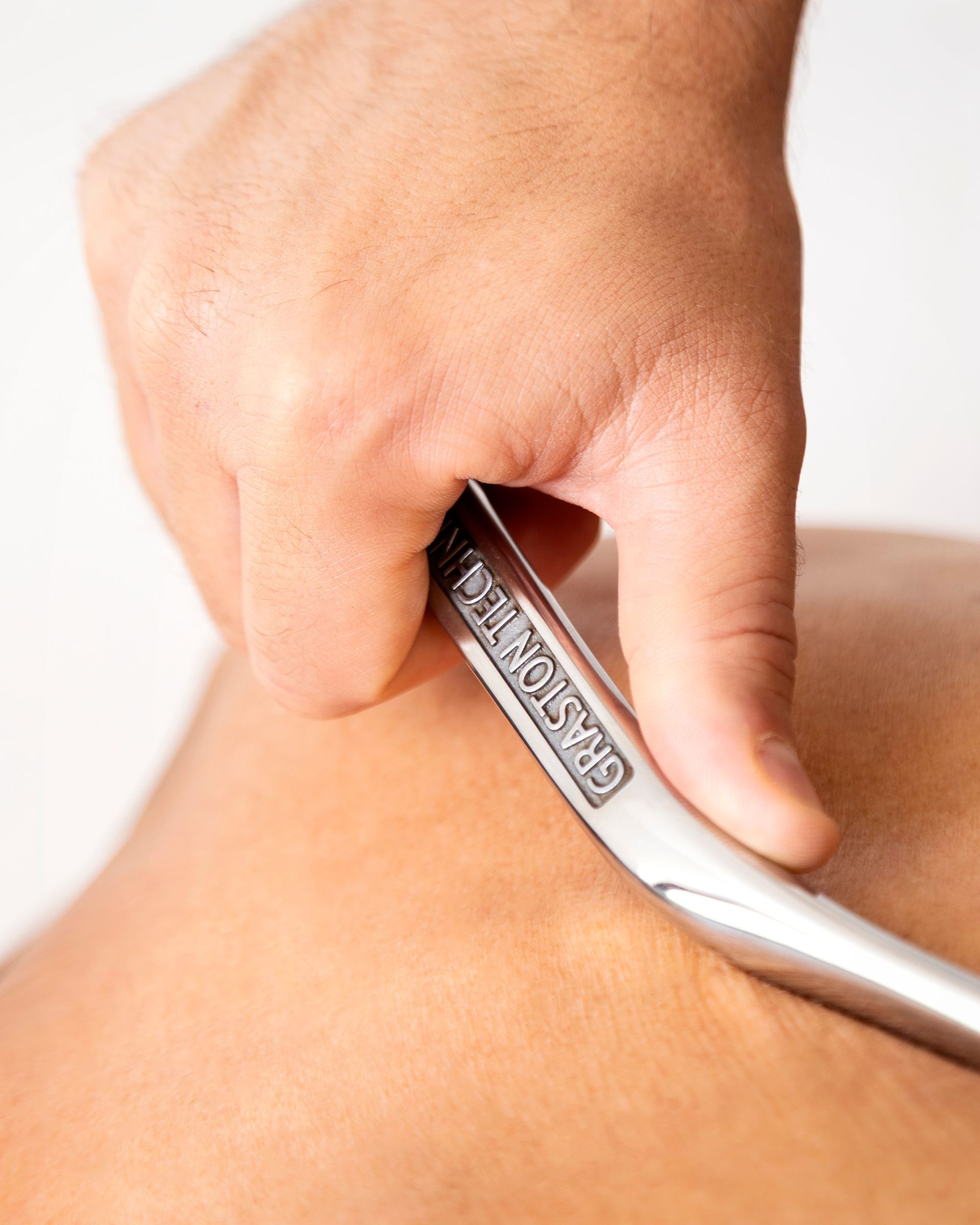 Mano di una persona che usa uno strumento metallico sulla schiena di un'altra persona, probabilmente per terapia muscolare.