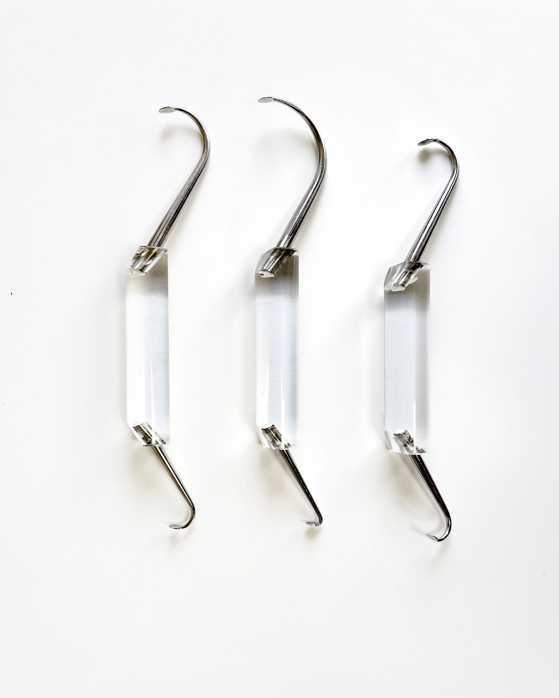 Tre sollevatori dentali con manici in plastica trasparente su una superficie bianca.