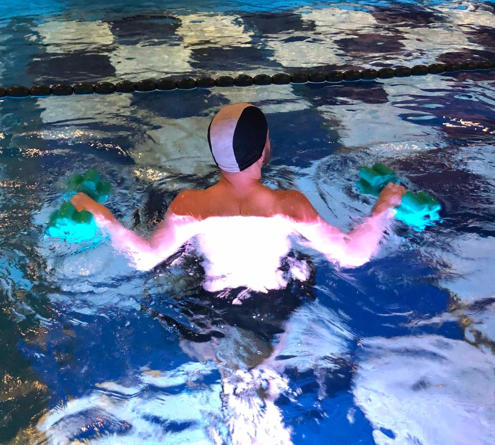 Persona in piscina con pesi turchesi, cuffia da nuoto, che fa acquagym.