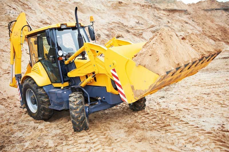 Una retroexcavadora amarilla llena de arena se encuentra en una obra en construcción.