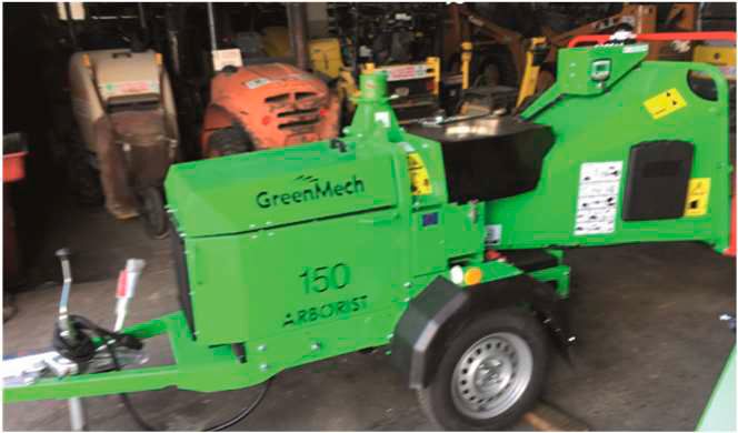 Un remolque triturador de madera GreenMech 150 Arborist de color verde estacionado en el interior, visto de lado.