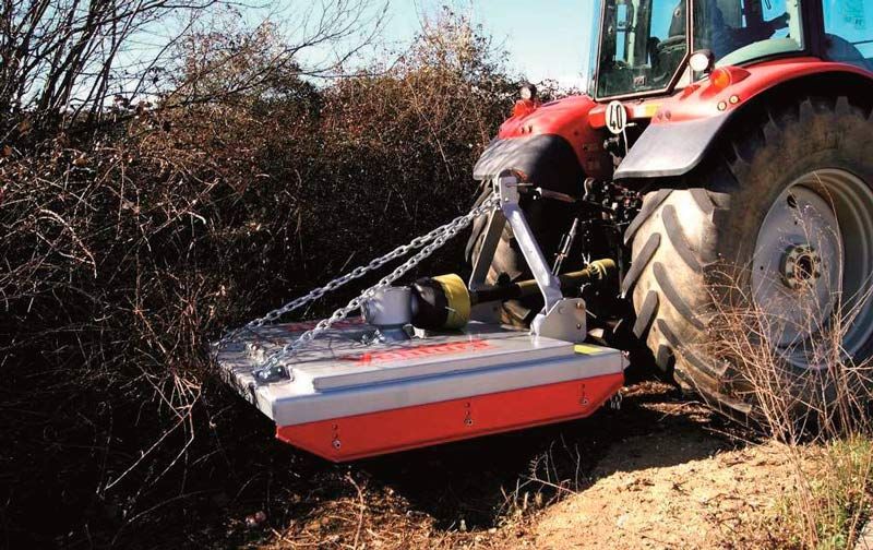 Un tractor rojo acciona una desbrozadora montada lateralmente para recortar la densa vegetación a lo largo de una zanja.