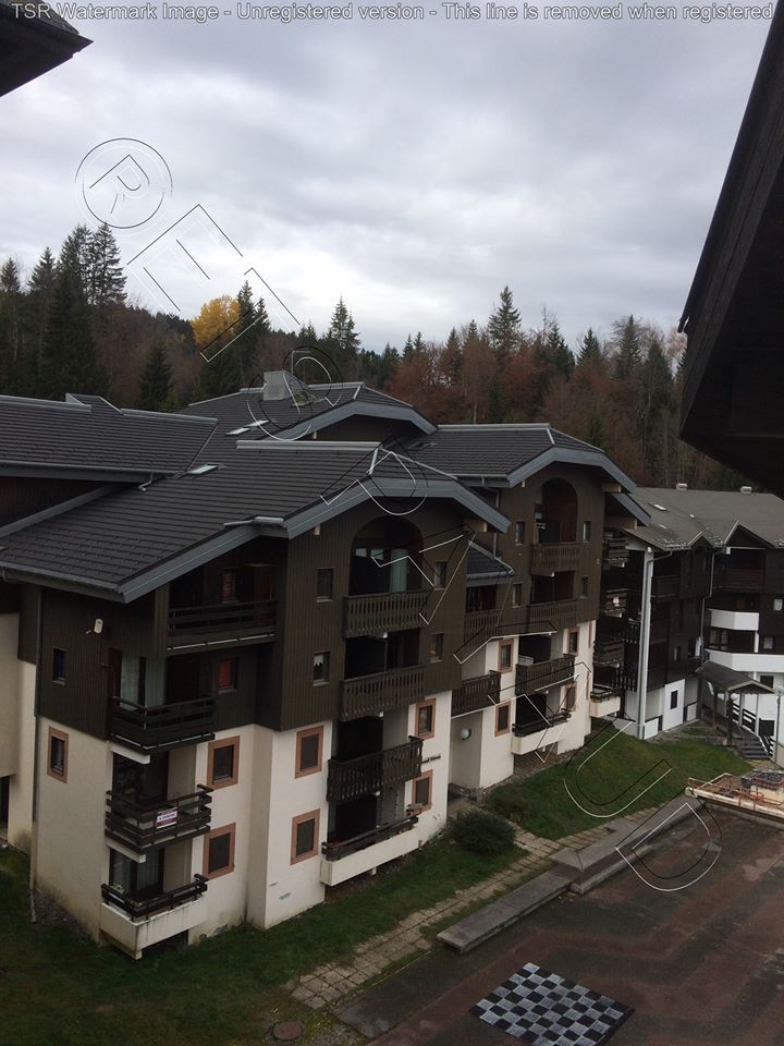 Immeubles d’appartements de montagne sous un ciel nuageux, près d’une cour mouillée et d’une forêt.