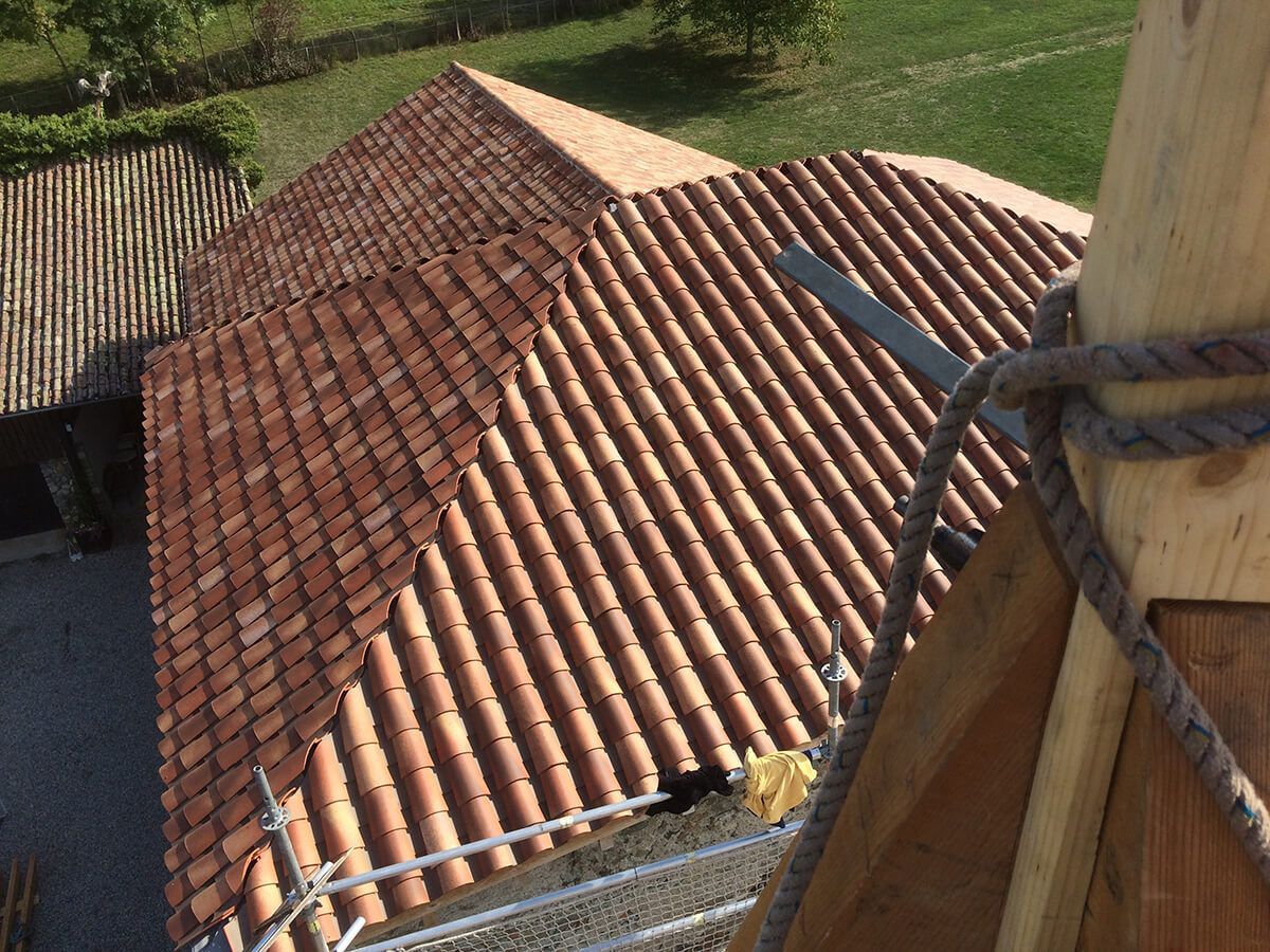 Toit en tuiles rouges vu d’en haut, à côté d’une structure en bois et d’une corde