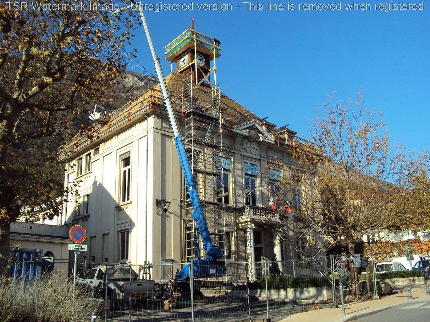 Une grue bleue près d’un bâtiment historique en cours de rénovation, à l’angle d’une rue ensoleillée