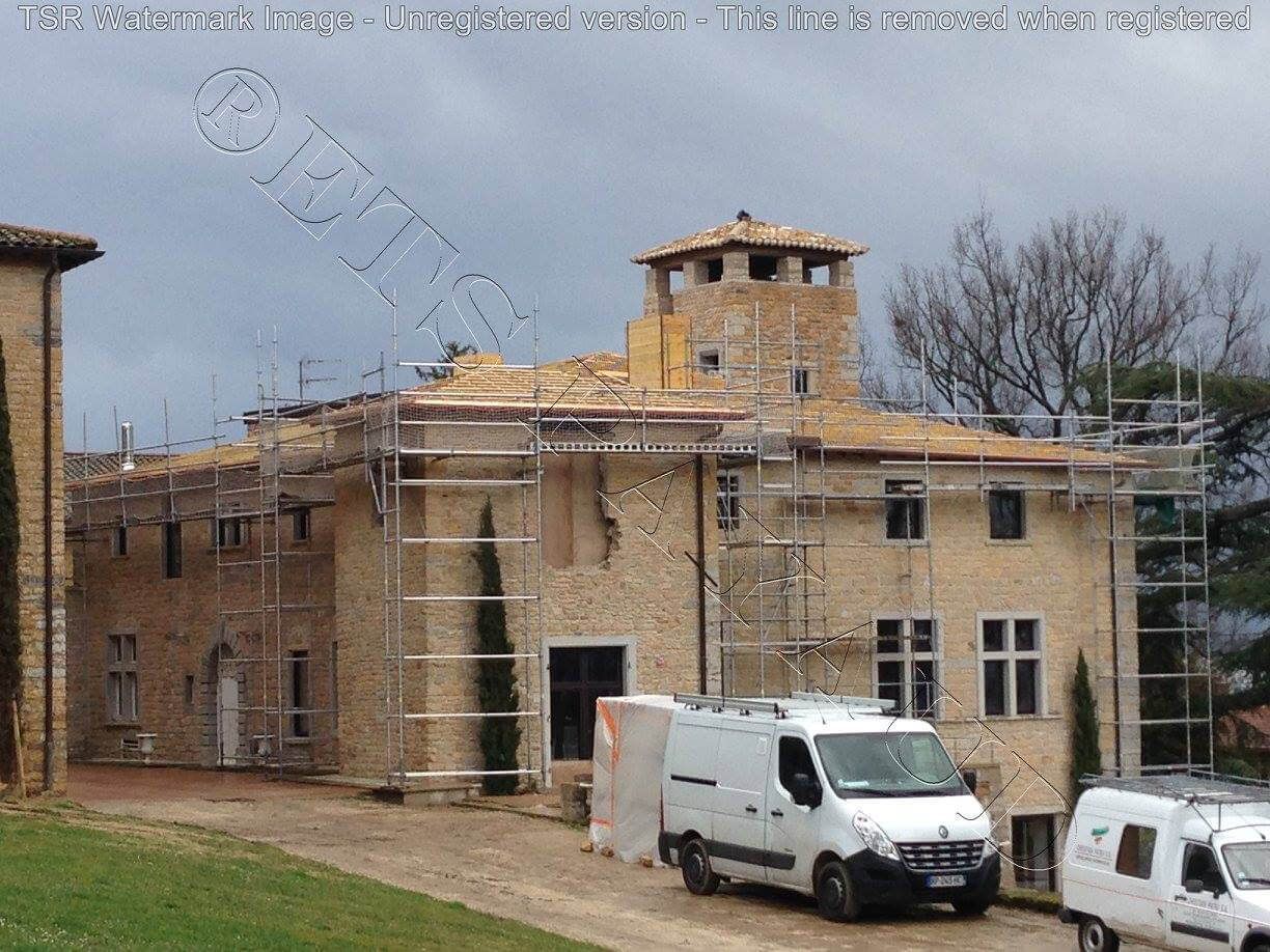 Maison en pierre en construction, avec un échafaudage et deux camionnettes blanches garées devant