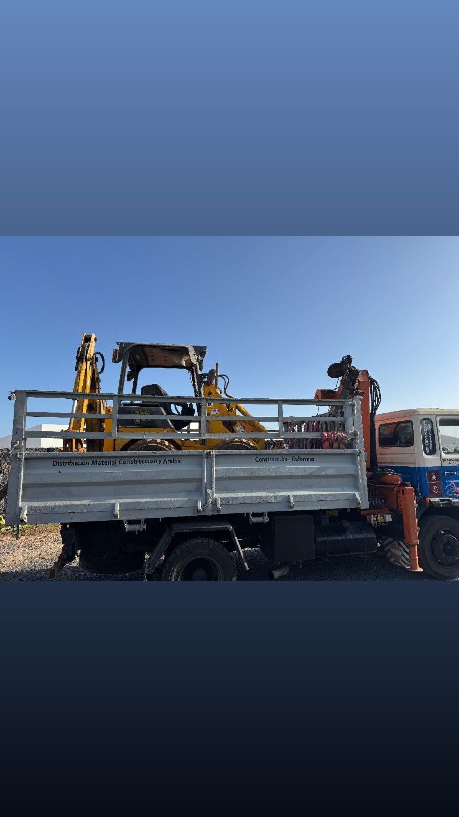 Trabajadores cargando maquinaria de construcción en un camión de plataforma en una obra al borde de la carretera.