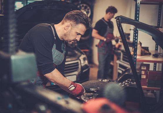 Dos mecánicos, vestidos con camisas oscuras y monos de trabajo, se concentran en reparar un vehículo en un taller mecánico bien equipado.