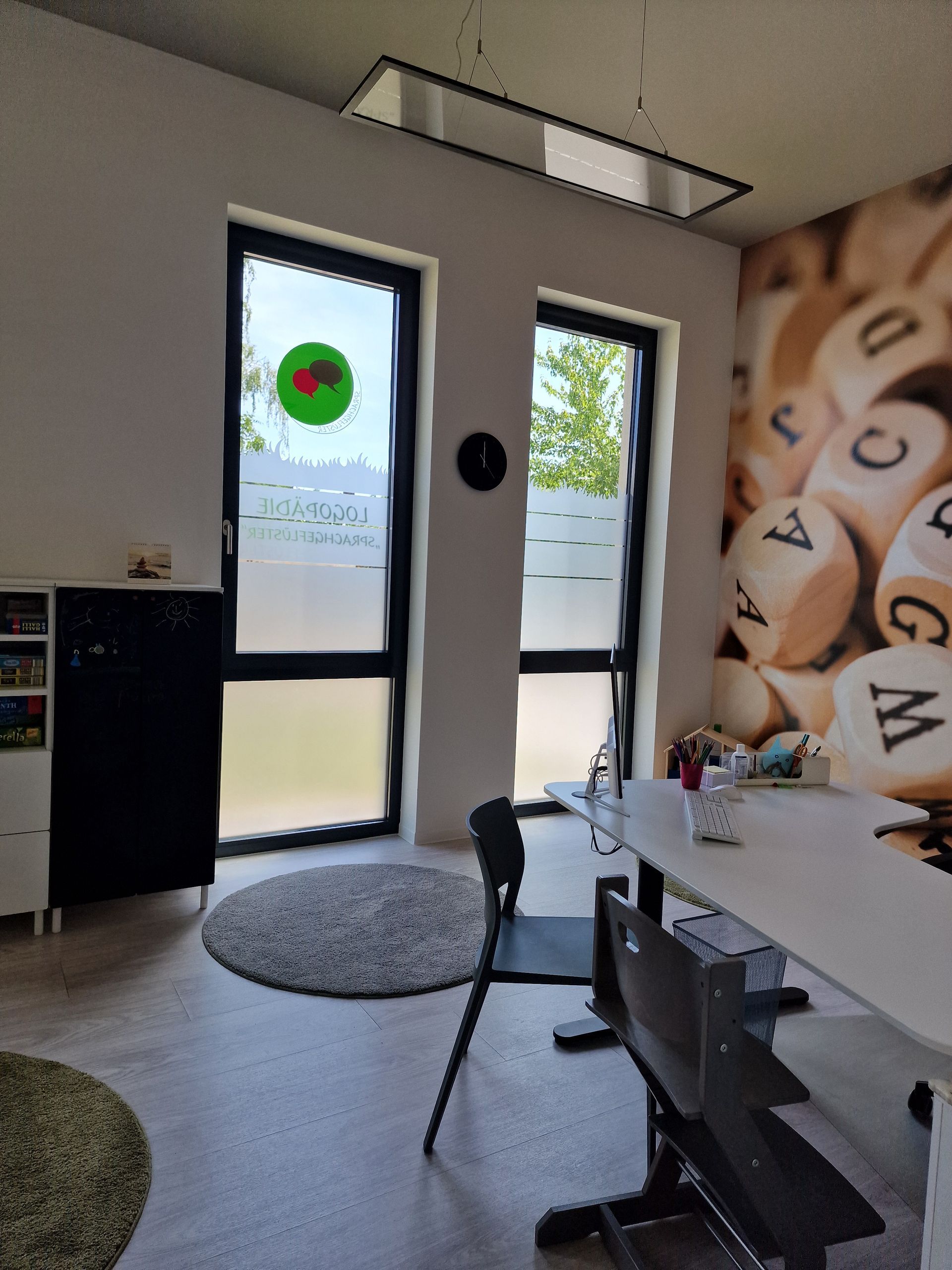 Holzspielzeug auf einem grünen Teppich vor einer grünen, grasähnlichen Wand: Perlenlabyrinthwagen, Aktivitätswürfel und Auto.