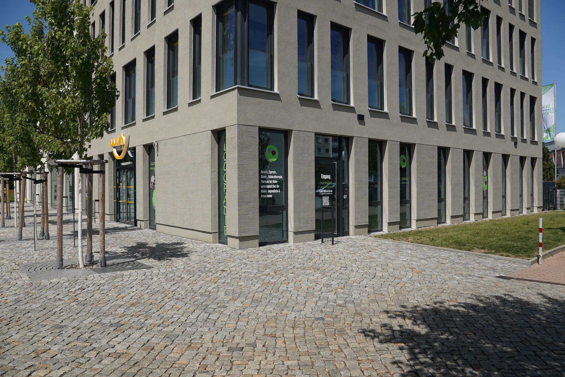 Beiges Mehrfamilienhaus mit Balkonen und dunklem Dach. Ecklage, Straßenschild sichtbar.