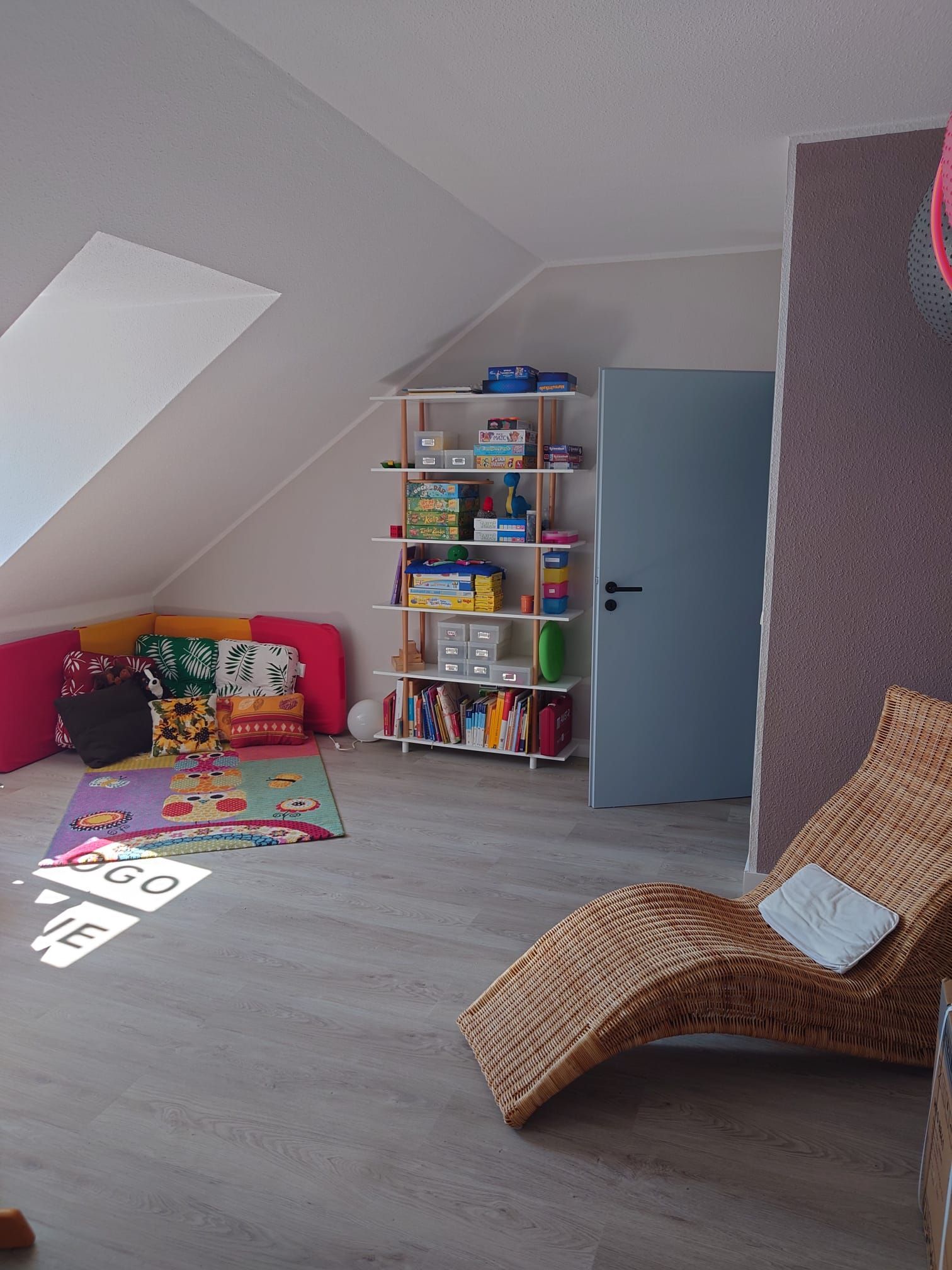 Heimbüro mit weißem Schreibtisch, lila Orchidee, bunten Stühlen und schräger Decke.