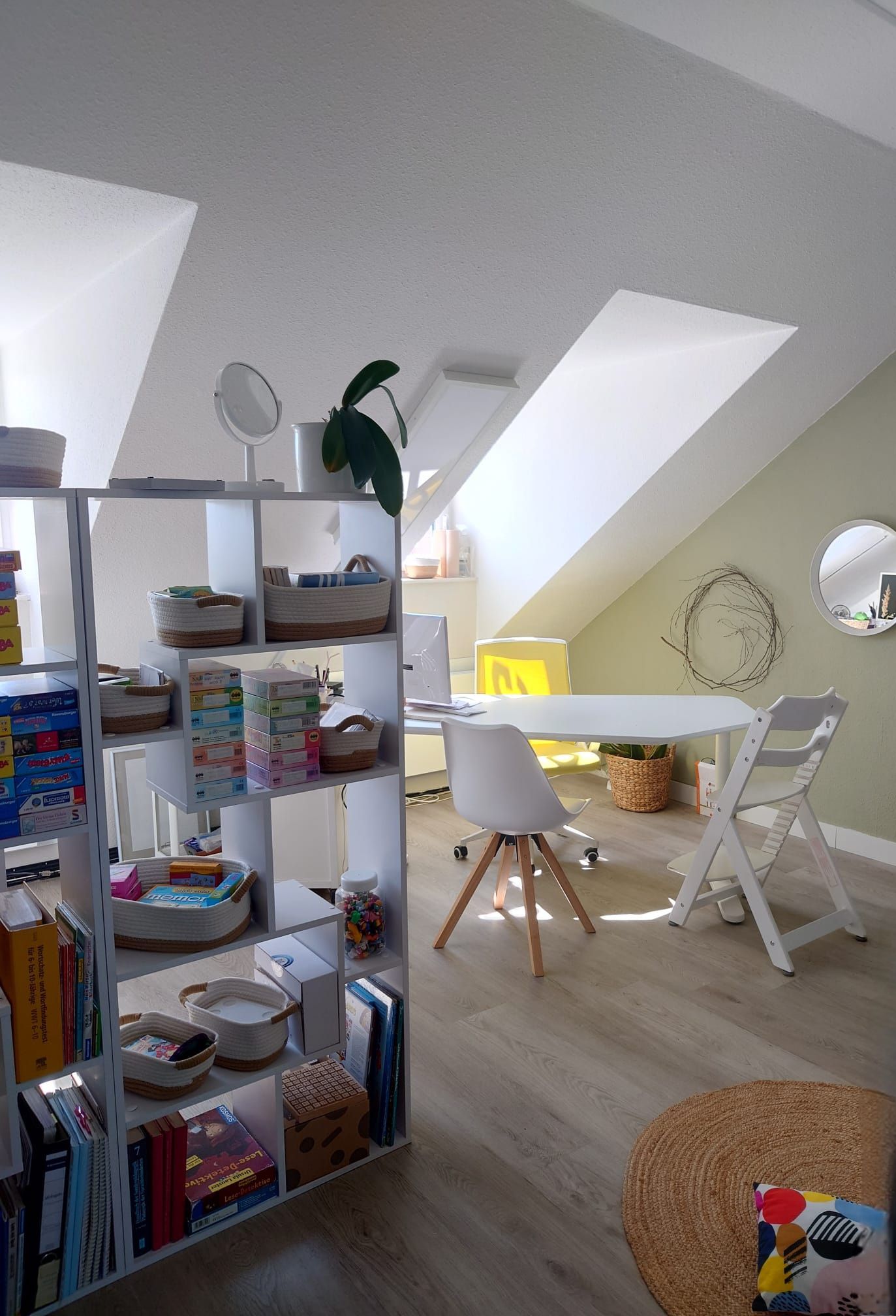 Büroraum mit schrägem Dach, Schreibtisch und Regalen, ausgestattet mit Stühlen und verschiedenen Spielsachen.