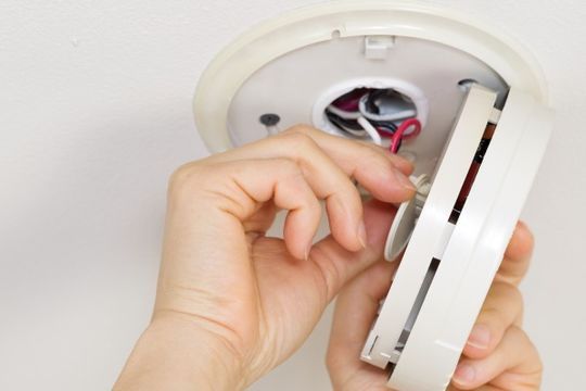 Elektroinstallateur schließt einen Rauchmelder an der Zimmerdecke an.