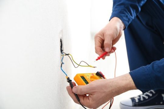 Installateur misst Spannung der Stromkabel in der Wand aus.