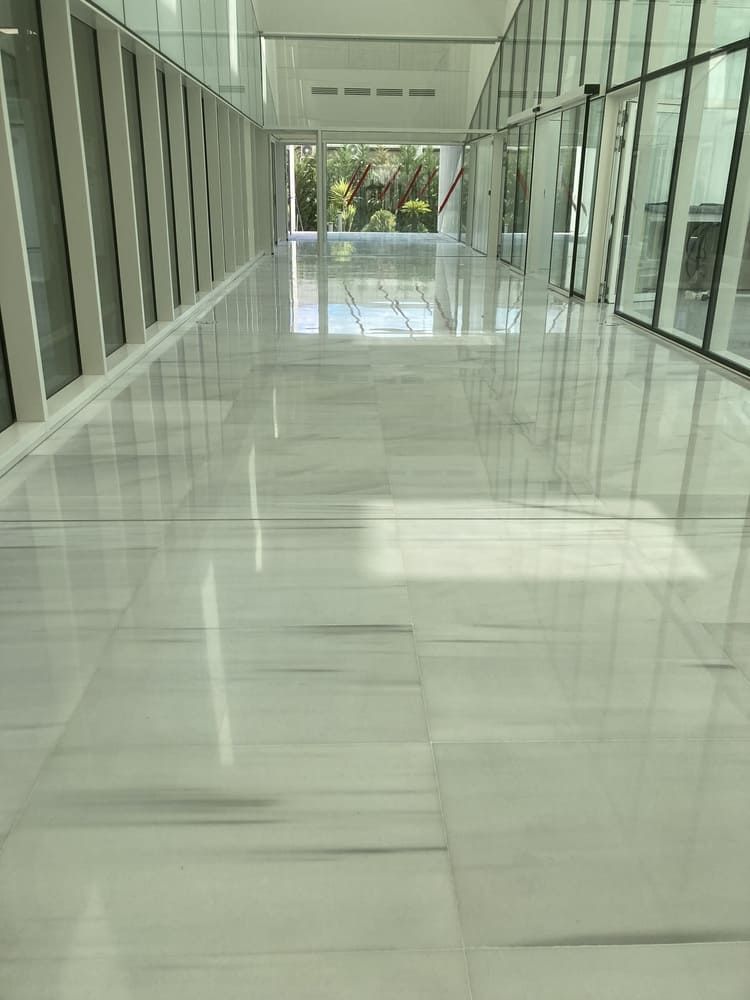 Un largo pasillo con azulejos blancos y muchas ventanas.