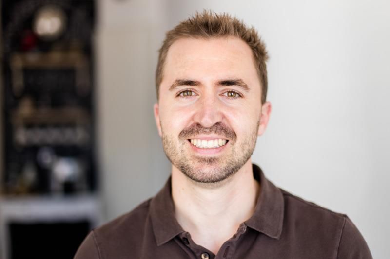 Ein Mann mit Bart und einem braunen Hemd lächelt in die Kamera.