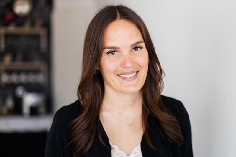 Eine Frau mit langen braunen Haaren lächelt und trägt eine schwarze Jacke.