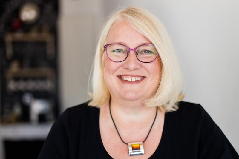 Eine Frau mit Brille und Halskette lächelt in die Kamera.