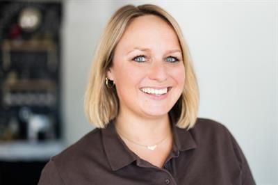 Eine Frau in einem braunen Hemd lächelt in die Kamera.