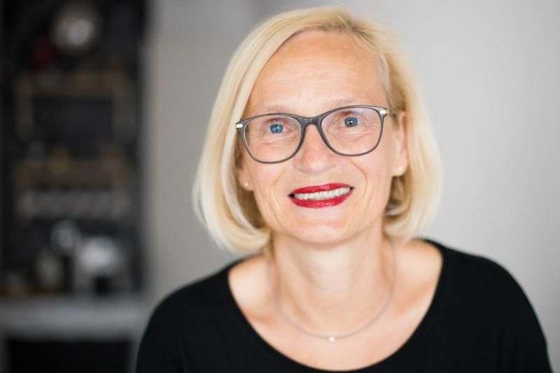 Eine Frau mit Brille und rotem Lippenstift lächelt in die Kamera.