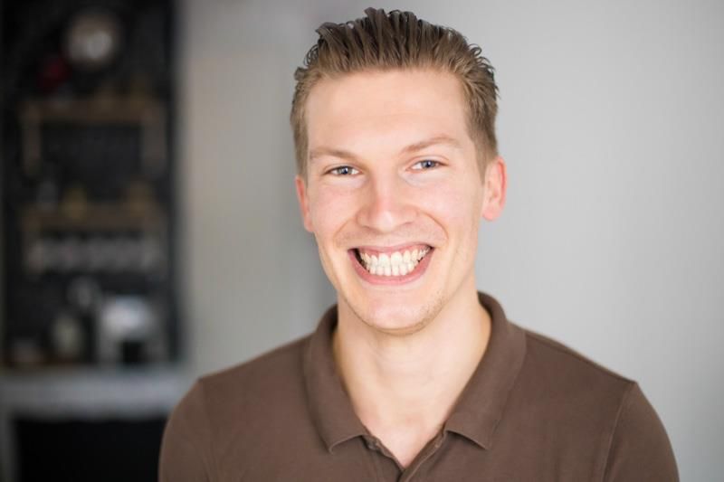 Ein junger Mann in einem braunen Hemd lächelt in die Kamera.