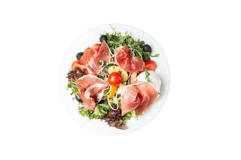 Salat mit Prosciutto, Tomaten, Oliven und Gemüse auf einem weißen Teller.