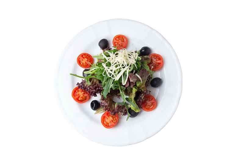 Salat mit Rucola, Tomaten, Oliven und geriebenem Käse auf einem weißen Teller.