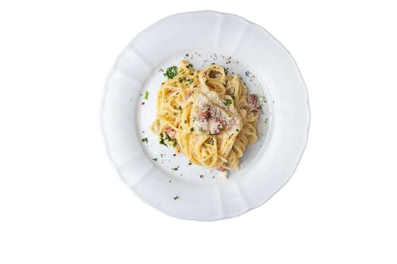 Pasta Carbonara in einer weißen Schüssel, garniert mit Petersilie und Pfeffer.
