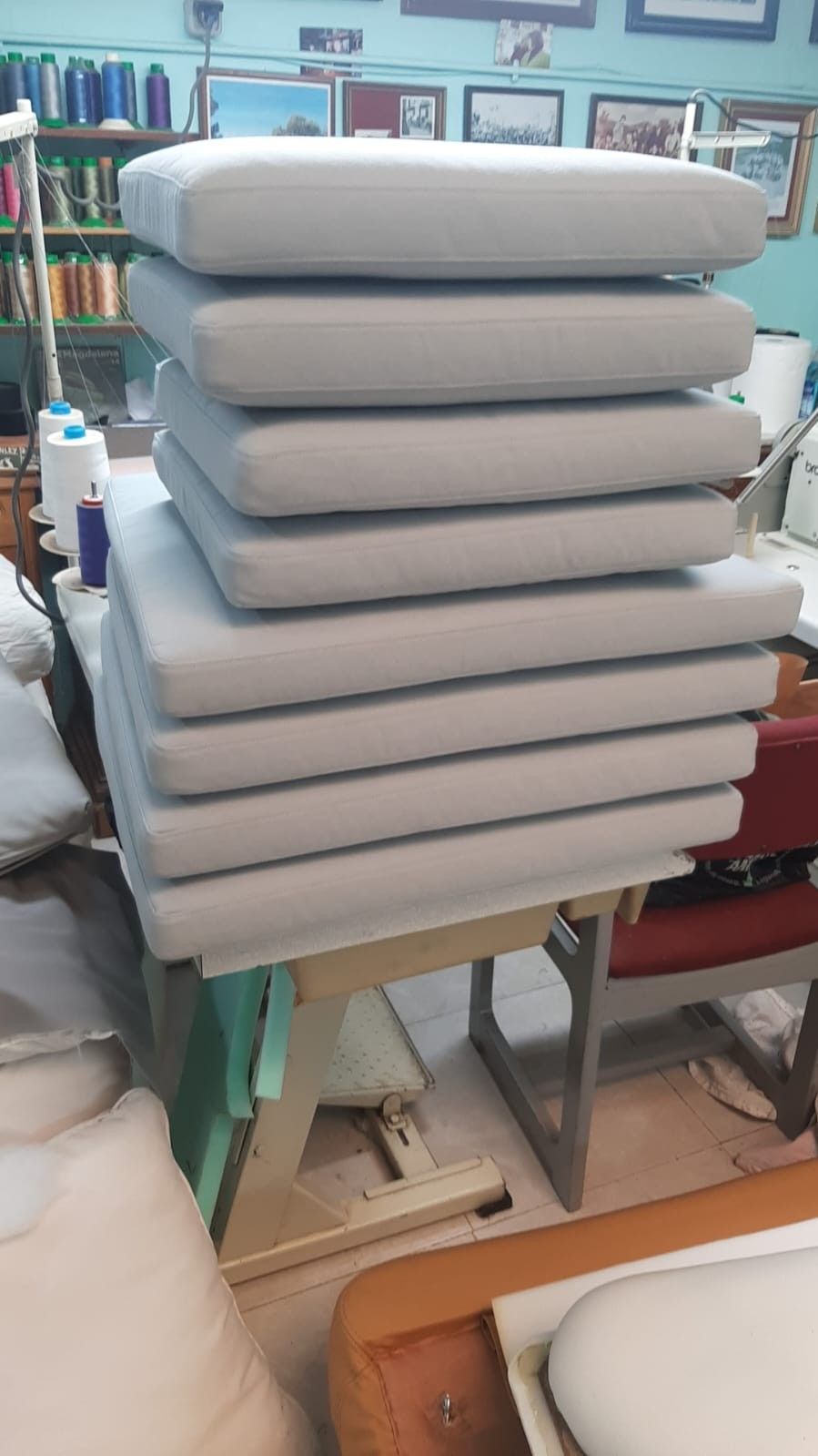 Una pila de ocho cojines rectangulares de color gris claro sobre una mesa de trabajo de madera en un taller de costura.