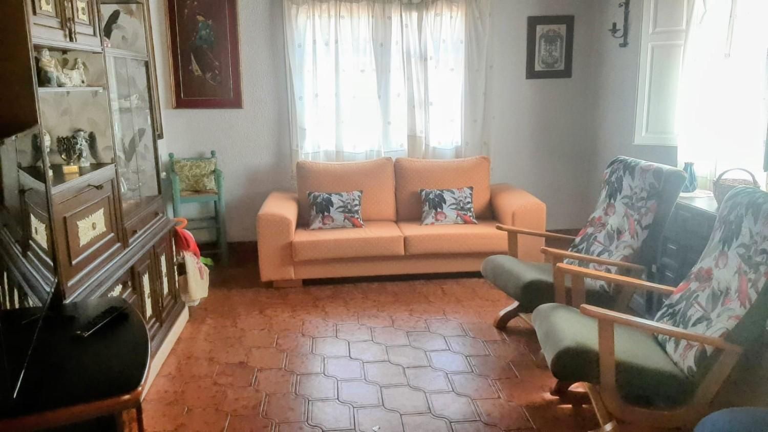 Una acogedora sala de estar con un sofá color melocotón, dos sillones con fundas estampadas y suelo de baldosas de terracota.