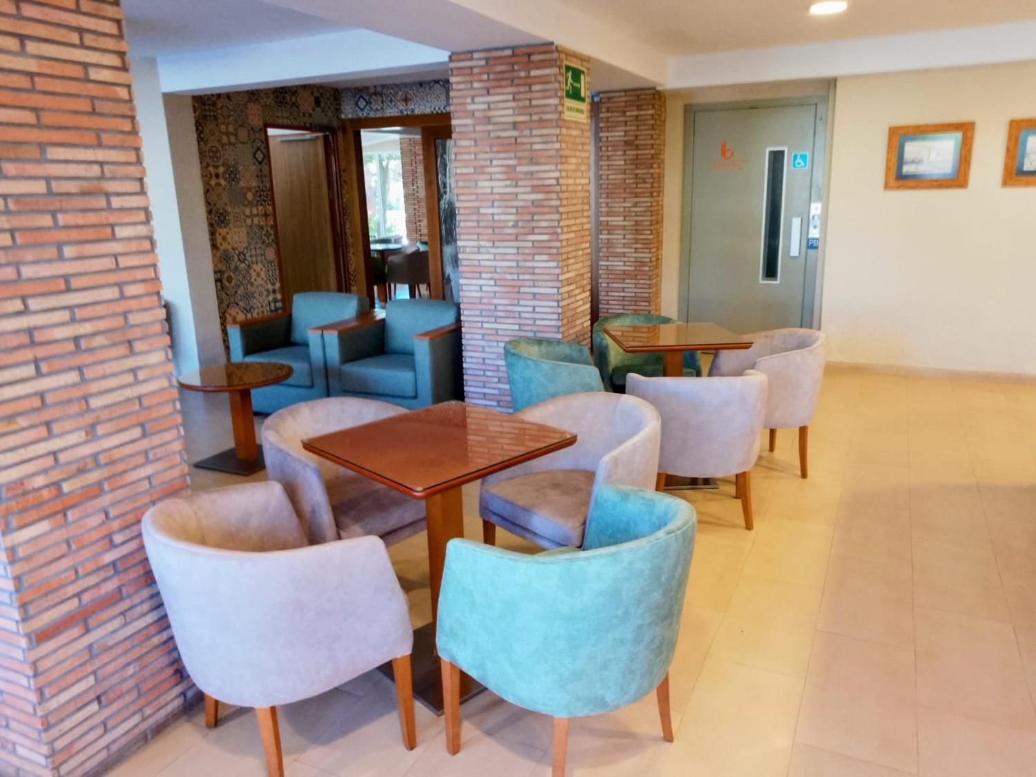 Una zona de estar con pilares de ladrillo, varios sillones tapizados en azul claro y beige, y pequeñas mesas de madera.