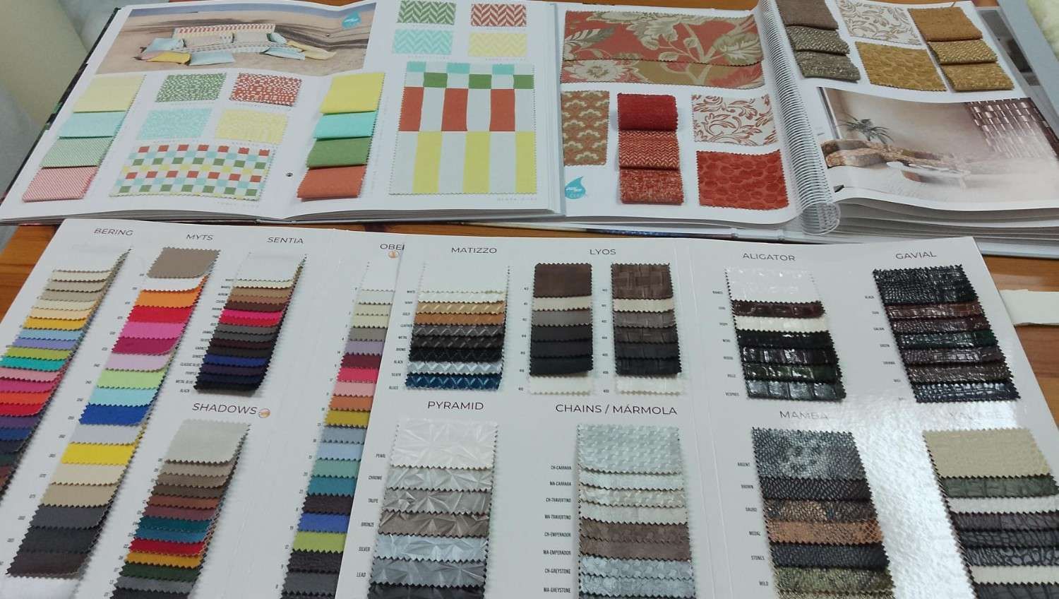 Una superficie cubierta de muestrarios de tela abiertos y tarjetas de muestras con diversos estampados, texturas y paletas de colores.