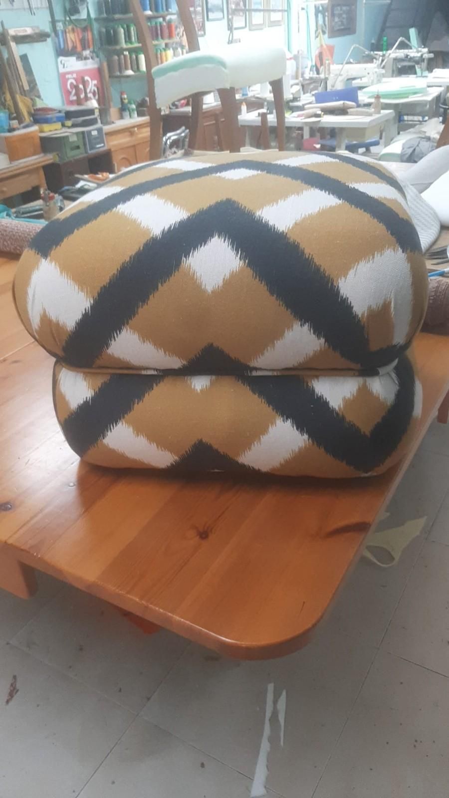 Dos cojines redondeados apilados con un estampado geométrico de espiga en marrón, negro y blanco sobre una mesa de madera.